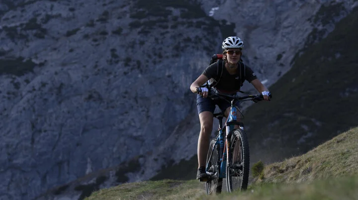 Eine Mountainbikerin fährt einen Trail in den Bergen hoch. | © DAV/Wolfgang Ehn
